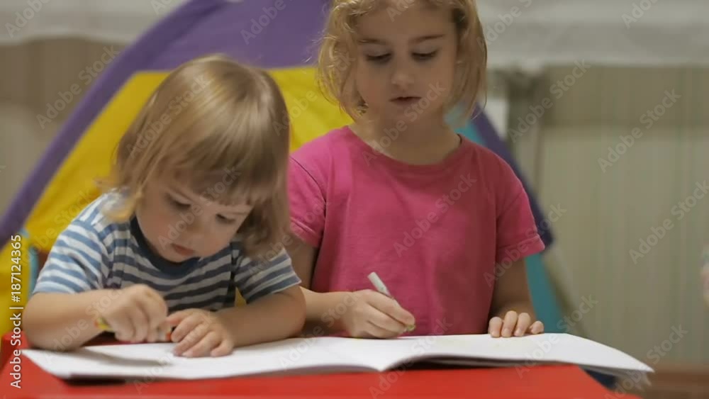 Two little children girl and boy sitting at table drawing. Brother and sister drawing with colorful crayons Two little children girl and boy sitting at table drawing. Brother and sister drawing with colorful crayons