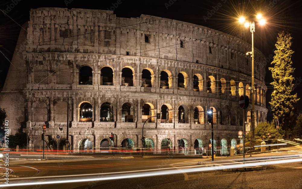 colosseum at night in rome italy with lamp reflection and traffic jam trail