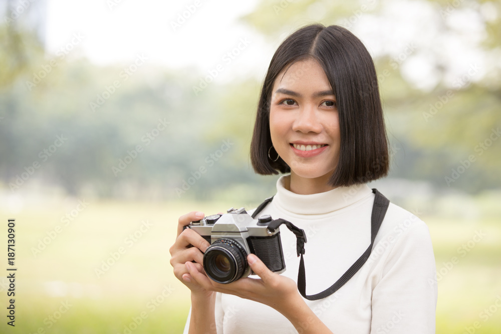 Attractive Asian shot hair woman holding retro camera with smiling, Woman using camera at outdoor place.