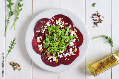 Schilderij op canvas Beetroot carpaccio with rucola leaves and pumpkin seeds on wooden white background