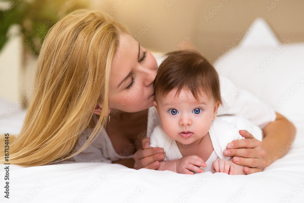 Adorable baby girl in white sunny bedroom have a tummy time. Newborn child relaxing on a bed with her mother Adorable baby girl in white sunny bedroom have a tummy time. Newborn child relaxing on a bed with her mother