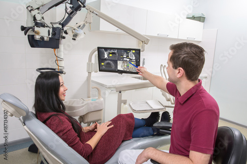 Dentist shows a patient x-ray of teeth. dental clinic. The patient is sitting in a chair. the dentist points the handle on the picture to the X-ray image on the monitor