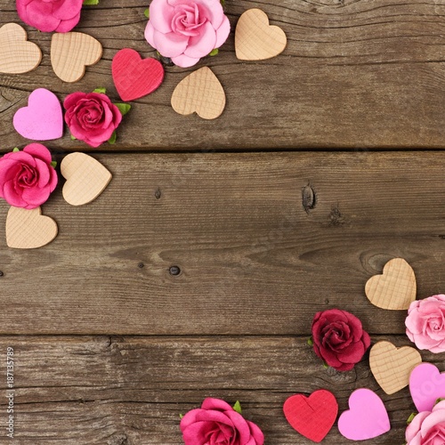 Valentines Day corner frame of wooden hearts and paper roses against a rustic wood background with copy space.