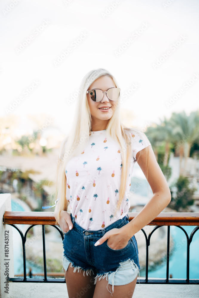 Happy blonde woman on balcony of hotel room on sky and palms backgrounds.