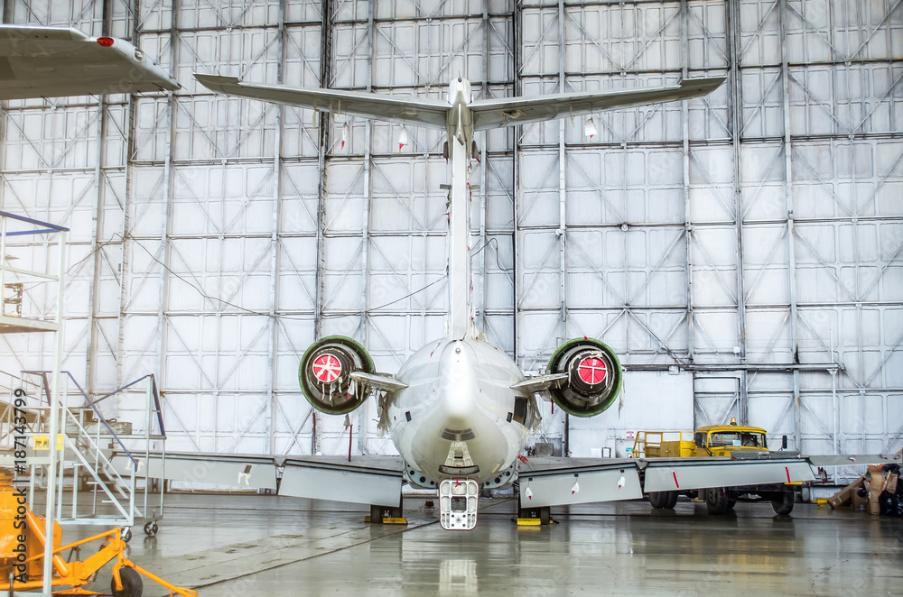 Passenger aircraft on maintenance of engine and fuselage repair in airport hangar. Rear view of the tail.