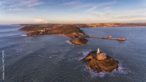 An early Winter sun lights up Mumbles Lighthouse, Bracelet Bay and Mumbles Pier in Swansea Bay, South Wales UK.