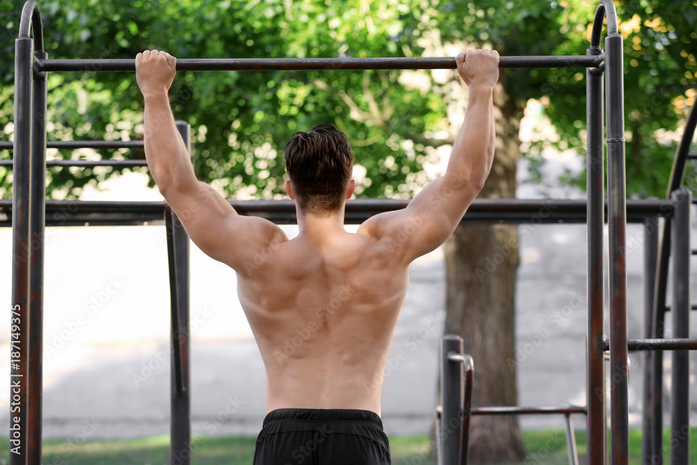 Handsome young man doing chin ups outdoors