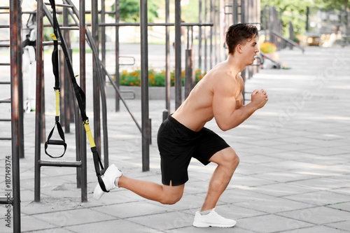 Handsome muscular young man exercising with TRX straps outdoors