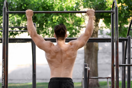 Handsome young man doing chin ups outdoors