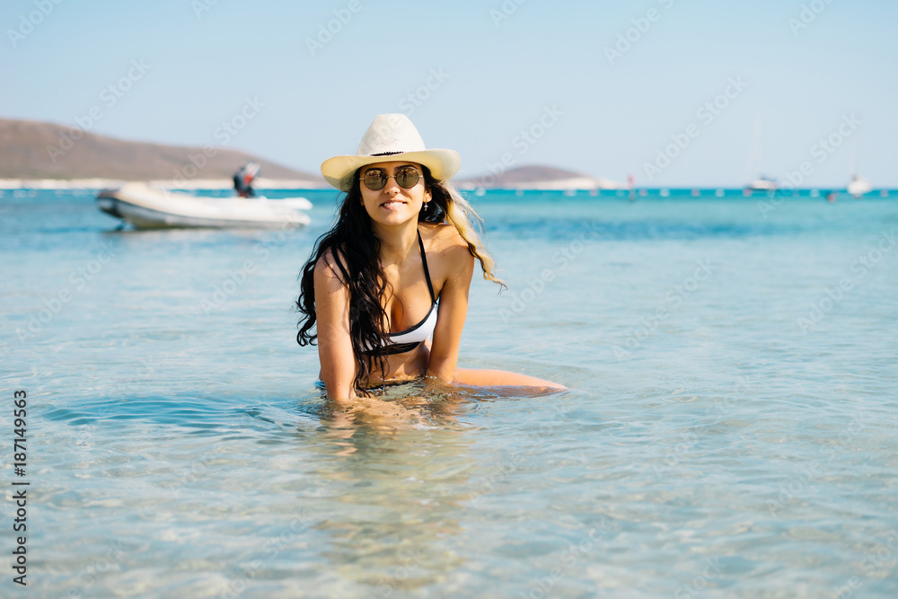 the girl in a hat smiles cute and sits in the sea
