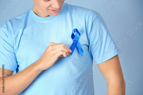 Canvastavla Young man wearing t-shirt with blue ribbon on color background, closeup