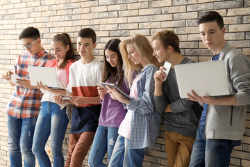 Group of cool teenagers with modern devices near brick wall
