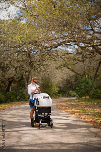 Young woman walking in the park with baby stroller. Happy mother with child in the carriage. Girl with a pram outdoors in the big park. © goodmoments