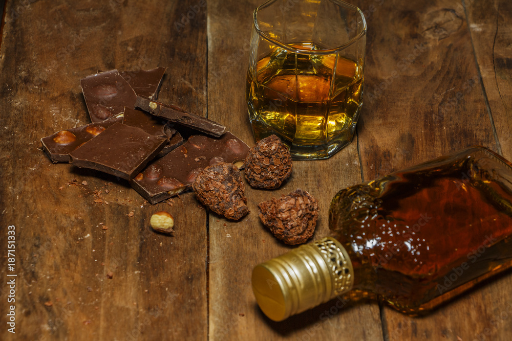 A glass of cognac or whiskey on a rustic table with chocolate and truffles. - obrazy, fototapety, plakaty 