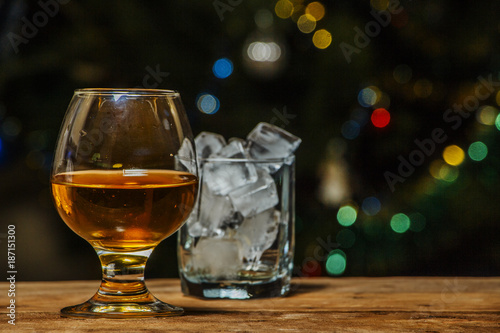 Fototapeta Naklejka Na Ścianę i Meble -  A glass of cognac or whiskey on a village table in the background of lights.