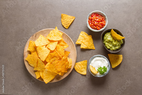 Snack for a party, chips with a tortilla, nachos with sauces: salsa with tomatoes, sour cream and guacamole. Mexican food. Dark background. Top view. Copy space