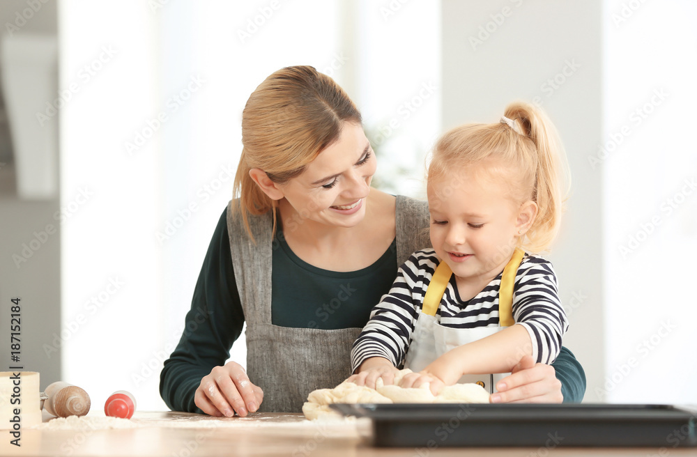 Mother and daughter with dough at table indoors Mother and daughter with dough at table indoors