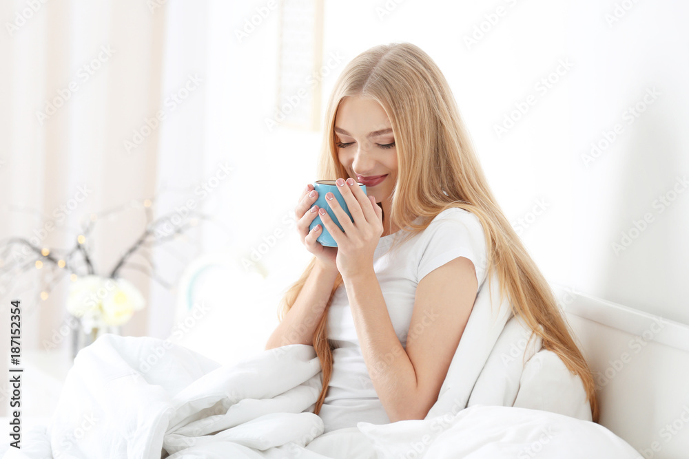 Young beautiful smiling woman with cup of coffee in bed at home Young beautiful smiling woman with cup of coffee in bed at home