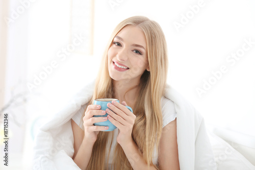 Young beautiful smiling woman with cup of coffee in bed at home