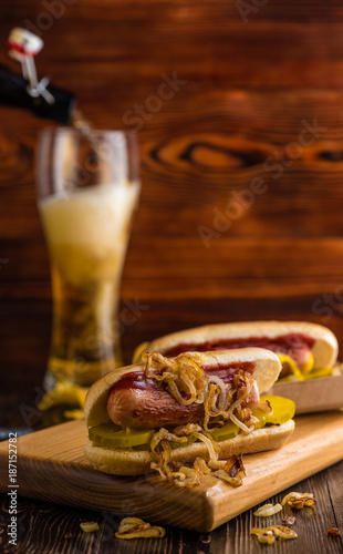 Hot dog with fried onions on a background of chips and beer on a wooden board