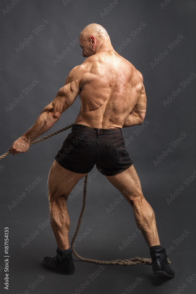 Back view of athletic man with great physique pulling rope. Stock