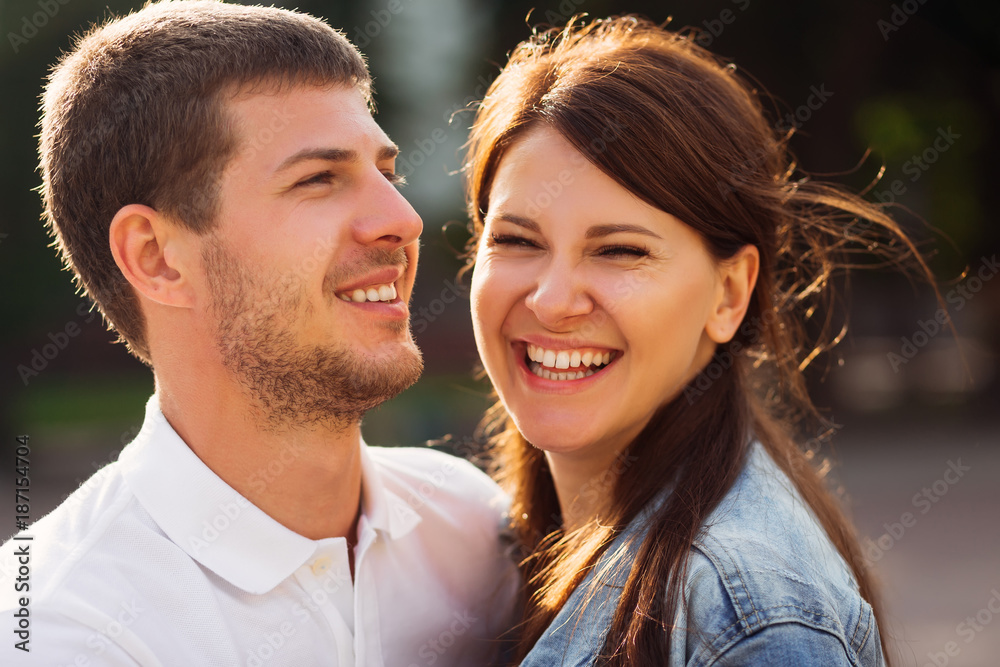 Fototapeta premium girlfriend laughs and looks into the camera lens and her boyfriend standing beside her and also smiling