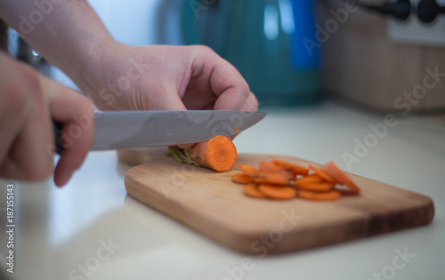 Chef is cutting carrot on a wooden cutting board with sharp knife