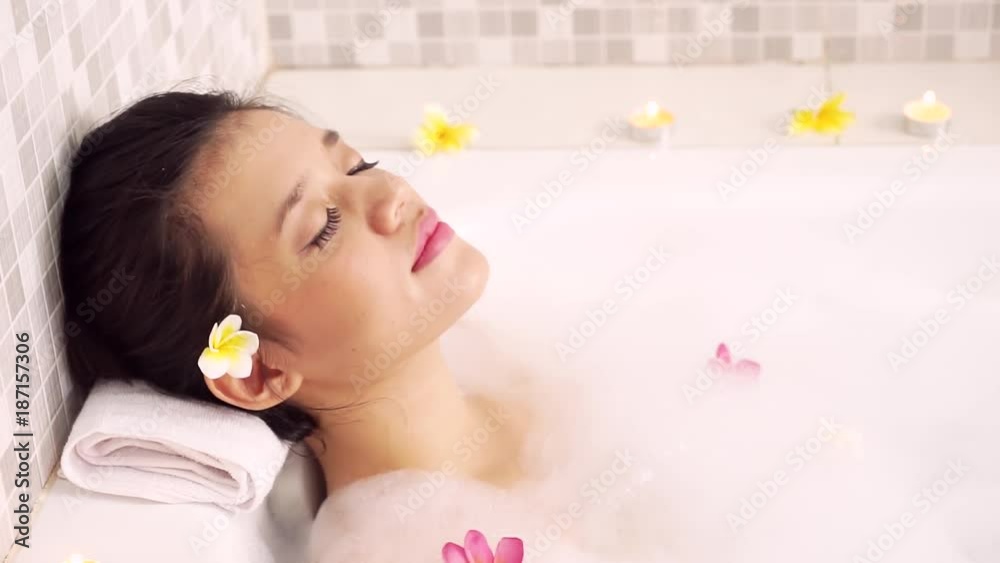 Spa concept. Beautiful young woman enjoying spa treatment in bathtub with foam and frangipani flowers Spa concept. Beautiful young woman enjoying spa treatment in bathtub with foam and frangipani flowers