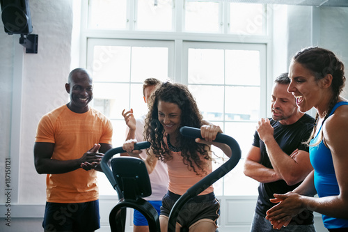 People cheering on their friend riding a health club bike