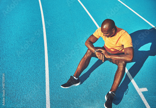 Young athlete sitting on a track checking his lap time