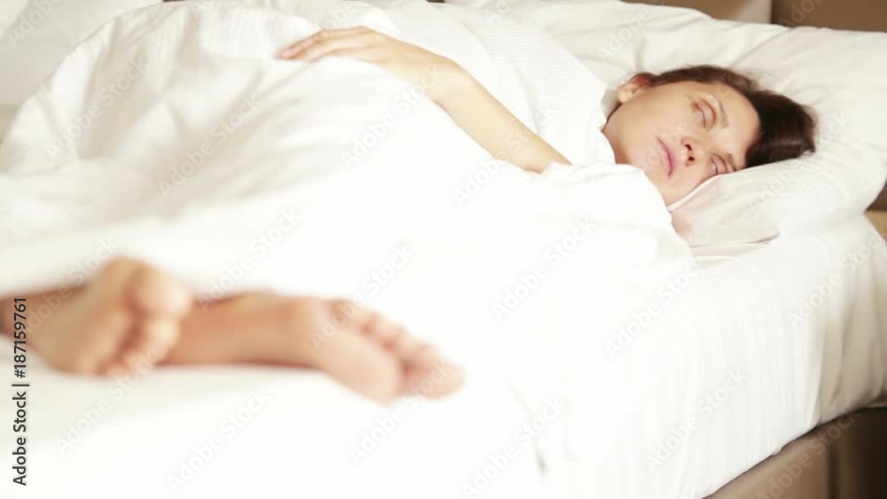 Woman peacefully sleeps in the morning with her feet showing from under the blanket Woman peacefully sleeps in the morning with her feet showing from under the blanket