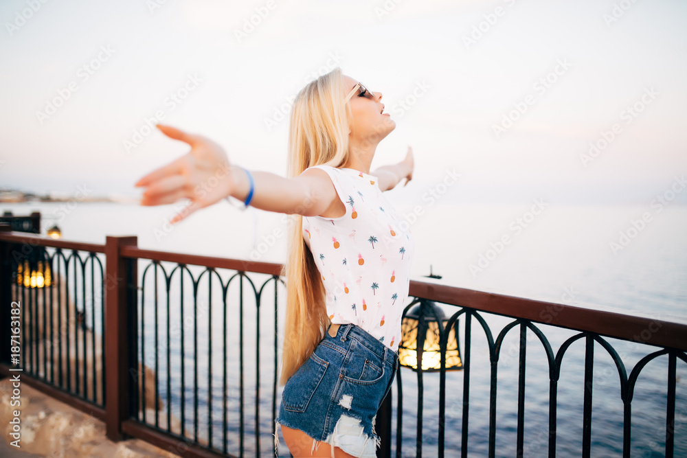 Woman stretching her arms to enjoy the fresh air of the sea at the balcony under cloudy sky. Summer vocation.