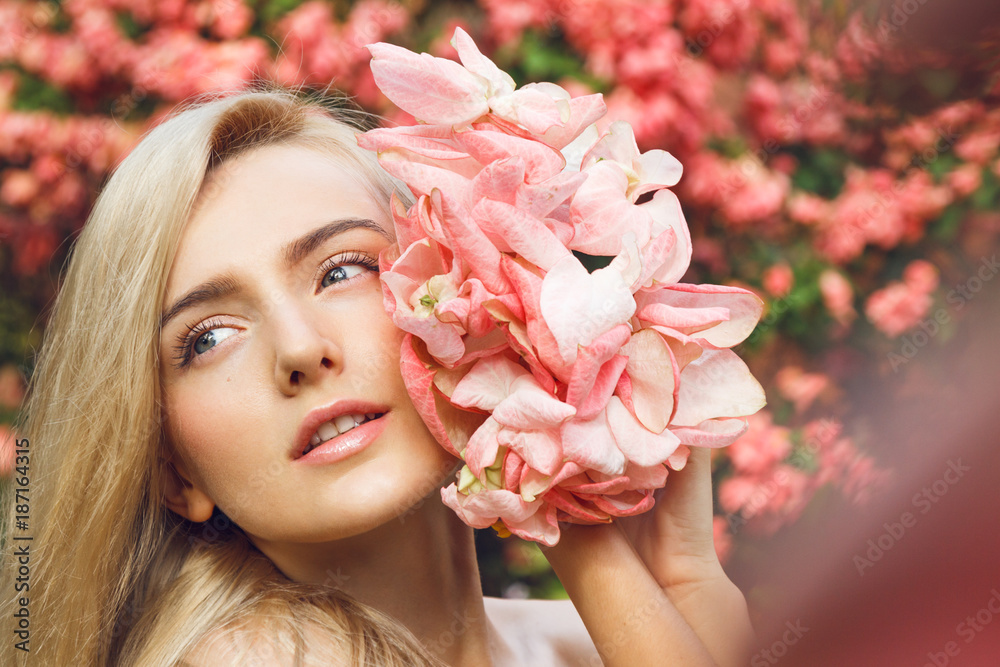 Close-up portrait of a beautiful young woman with long blonde hair, perfect skin and beautiful green eyes in a pink floral garden Close-up portrait of a beautiful young woman with long blonde hair, perfect skin and beautiful green eyes in a pink floral garden