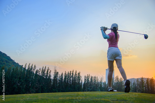 a woman golf player in an action at the ene of downswing, after hit the golf ball away from tee off to the fairway ahead by wood driver