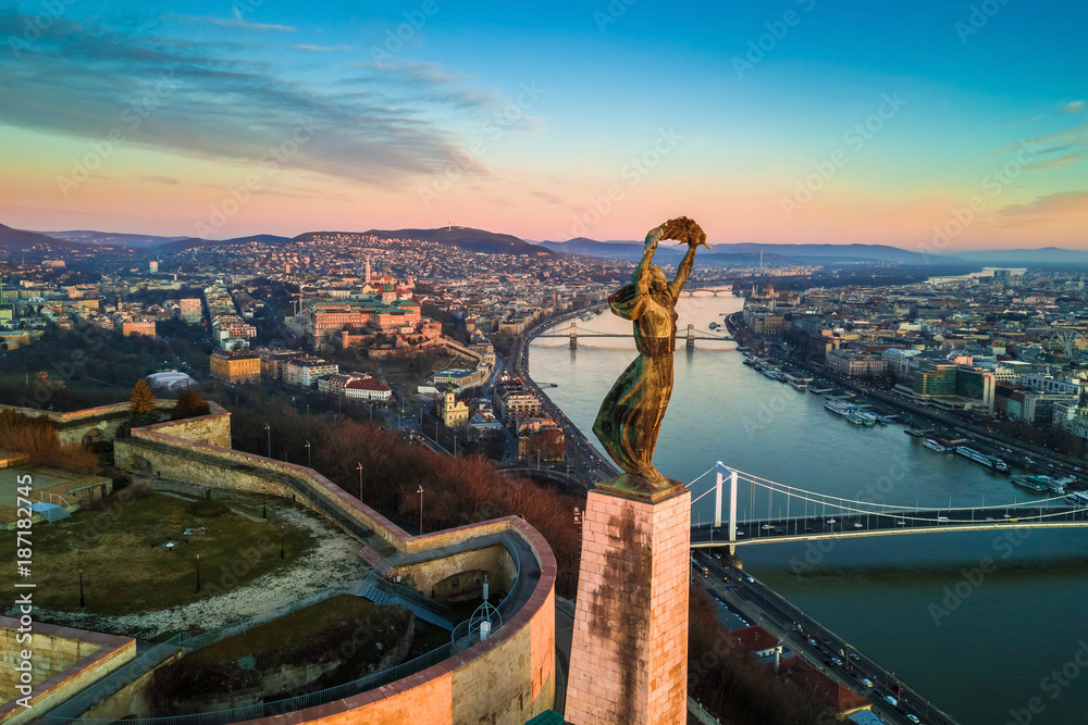 Obraz premium Budapest, Hungary - Aerial skyline view of Statue of Liberty with Buda Castle Royal Palace and Chain Bridge at background. Morning sunrise with blue sky and clouds