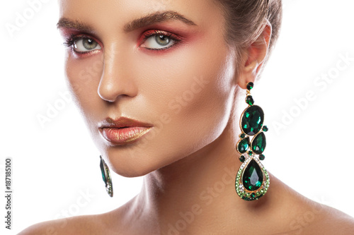 Beautiful woman with a colorful makeup is wearing earrings with green emeralds