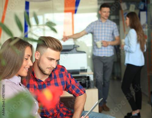 Two confident young people looking at touchpad while their colleagues working in the background. photo