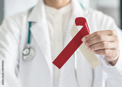 Burgundy ivory ribbon awareness on doctor’s hand, symbolic bow color for head and neck cancer, oral squamous cell carcinoma, throat, laryngeal and pharyngeal cancer