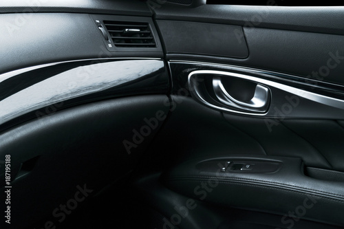 Car black perforated leather interior details of door handle with windows controls and adjustments. Car door handle inside the luxury modern car. Switch button control