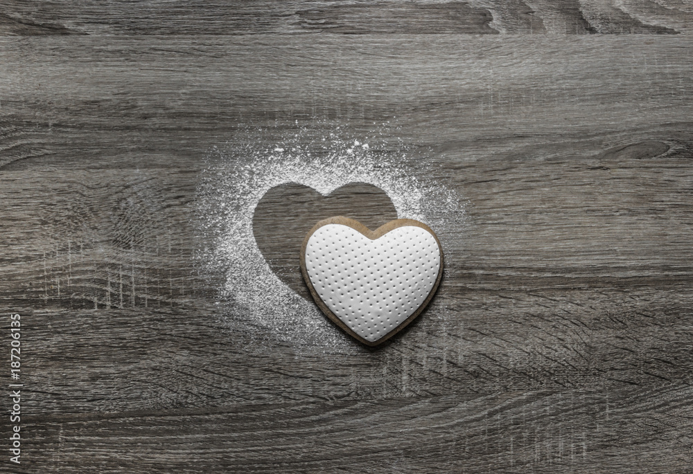 on a wooden background with powdered powder snow a silhouette of the heart is poured and below on the silhouette lies a cookie in the form of a heart on a wooden background with powdered powder snow a silhouette of the heart is poured and below on the silhouette lies a cookie in the form of a heart