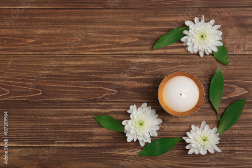 Composition with burning candle and flowers on wooden background, top view