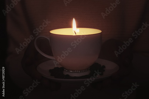 Woman holding cup with burning candle in darkness, closeup