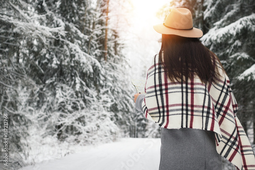 Handsome woman traveling in  winter holidays around snowy forest and hold map in hand. Wearing hat and scarf