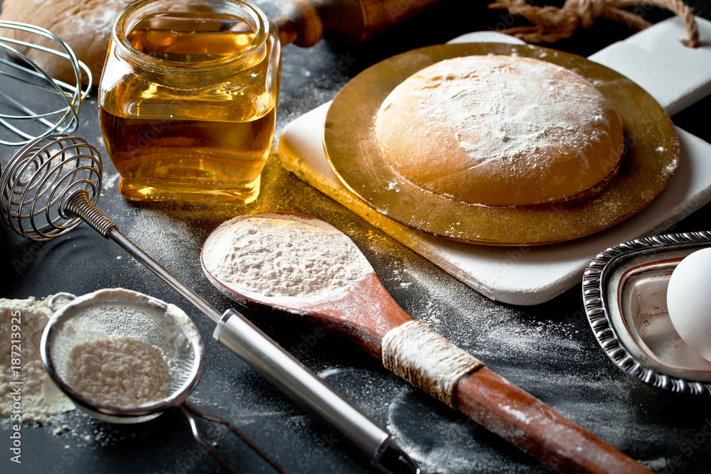 Fototapeta premium Dough with flour on an old background in a composition with kitchen accessories