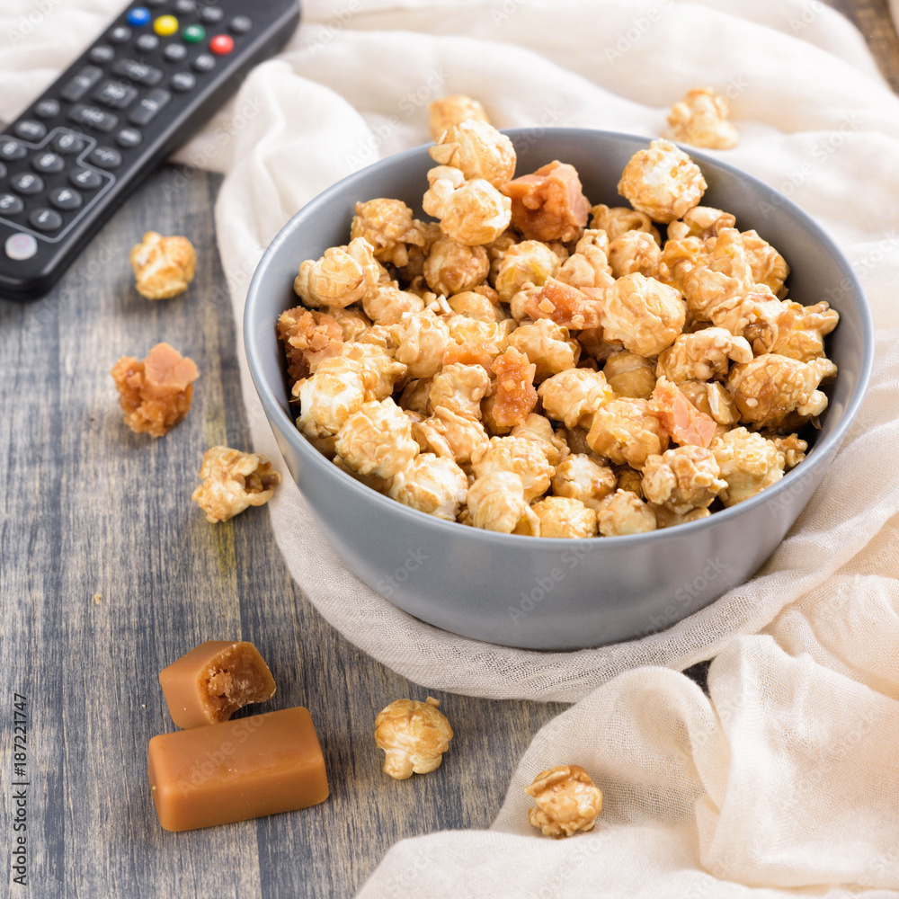 Bowl of a caramel popcorn. Homemade golden sweet corn on wooden grey table. TV remote control Bowl of a caramel popcorn. Homemade golden sweet corn on wooden grey table. TV remote control