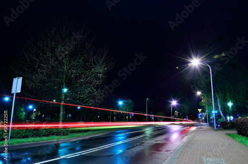 Ulica w mieście w nocy oświetlona lampami i smugi świateł samochodów.