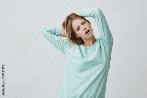 Positive female with appealing appearance and blonde dyed hair has cheerful expression, wears light blue sweater, rejoices having weekends, poses at camera. Pleasant emotions concept © Cookie Studio