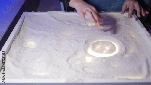 A young mother plays with her son in a salt room. Together they draw patterns on a luminous table.