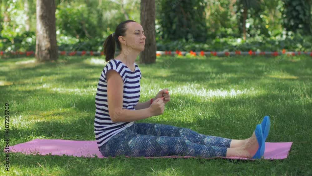 Beautiful young woman doing stretching yoga exercise on green grass at park