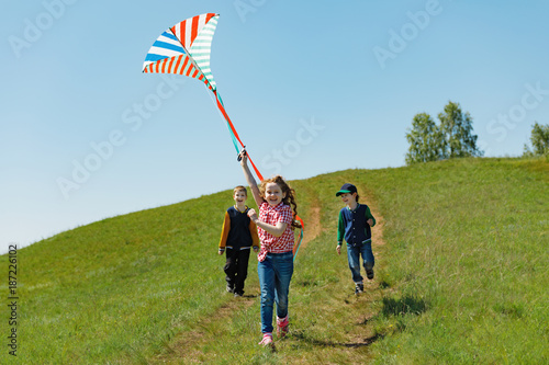 Children enjoy playing with a flying kite in meadow on sunny day.